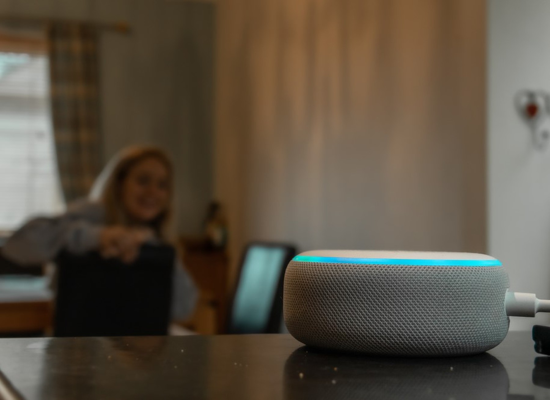 Altavoz inteligente Amazon Echo Dot en blanco con la luz azul de arriba iluminada porque se ve que al fondo una chica le está hablando