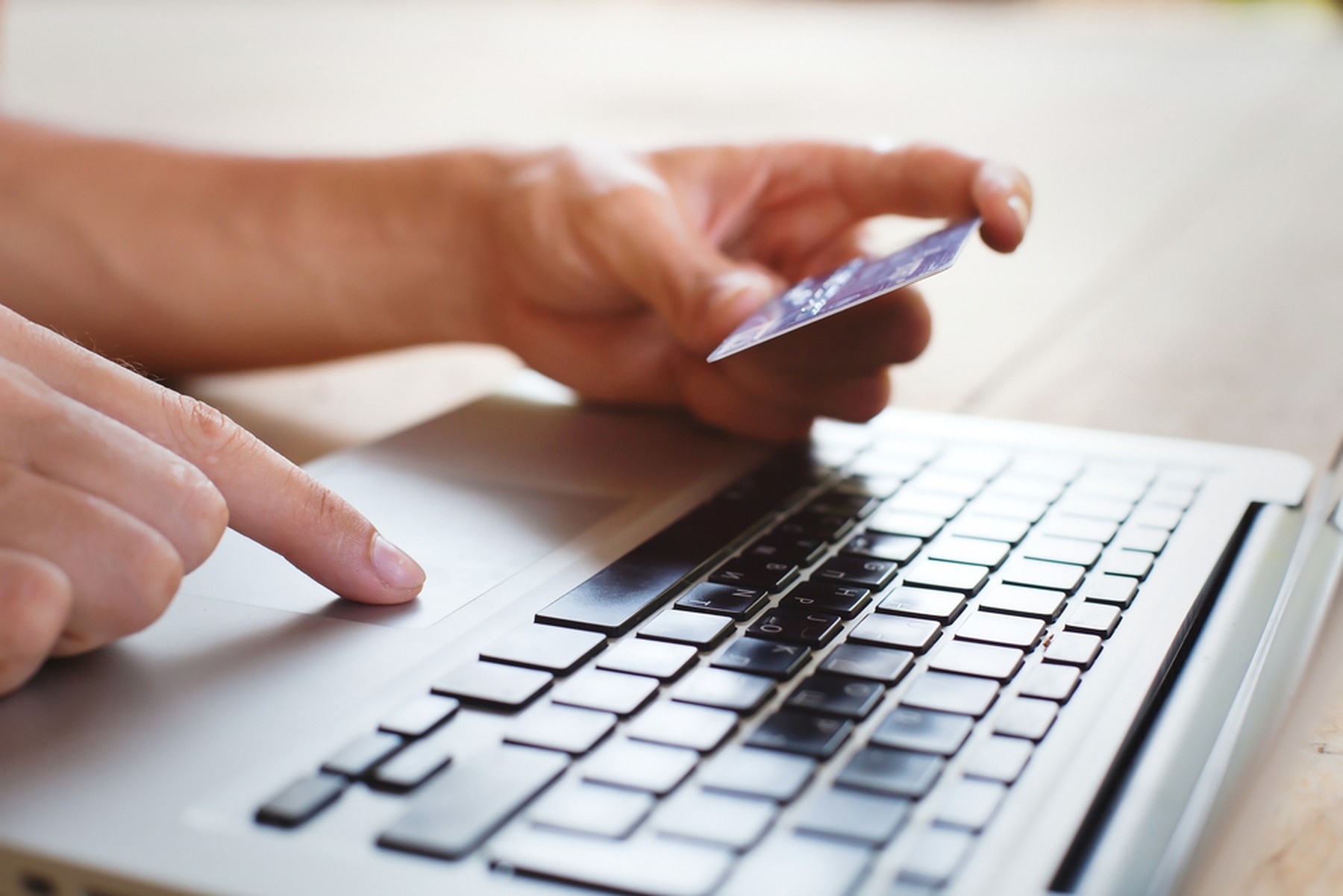 Manos de una persona utilizando su tarjeta de crédito para comprar online. Se ve también el teclado de un portátil.