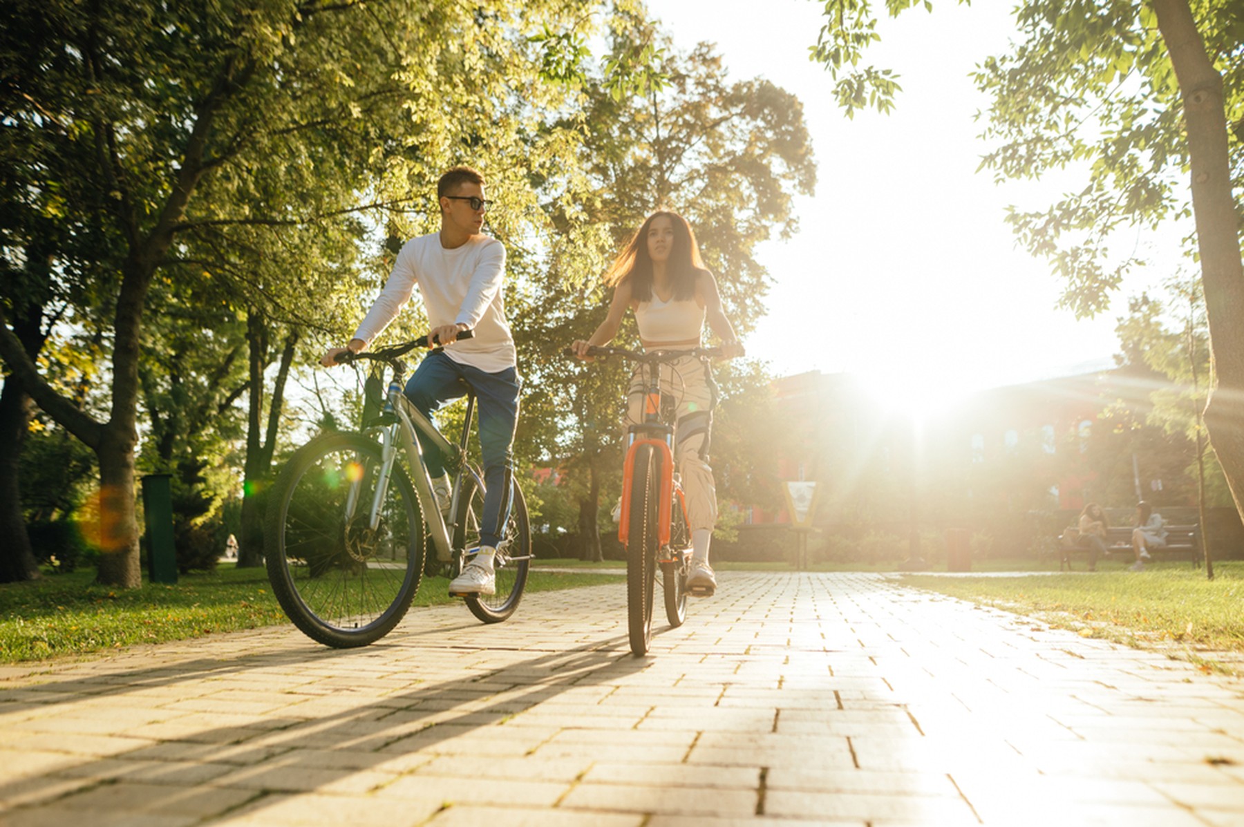 Chico y chica joven montando en bicicleta por un parque con el sol de espaldas
