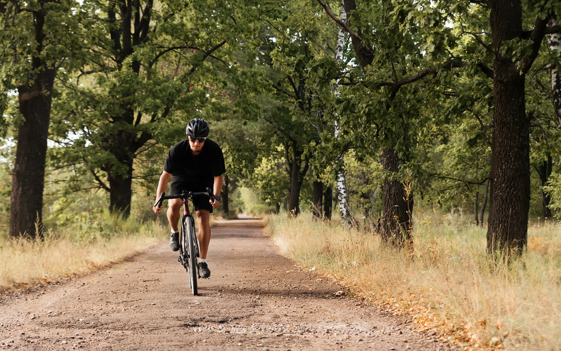 Hombre joven con una bicicleta de gravel pedalenado por un camino de tierra con árboles alrededor