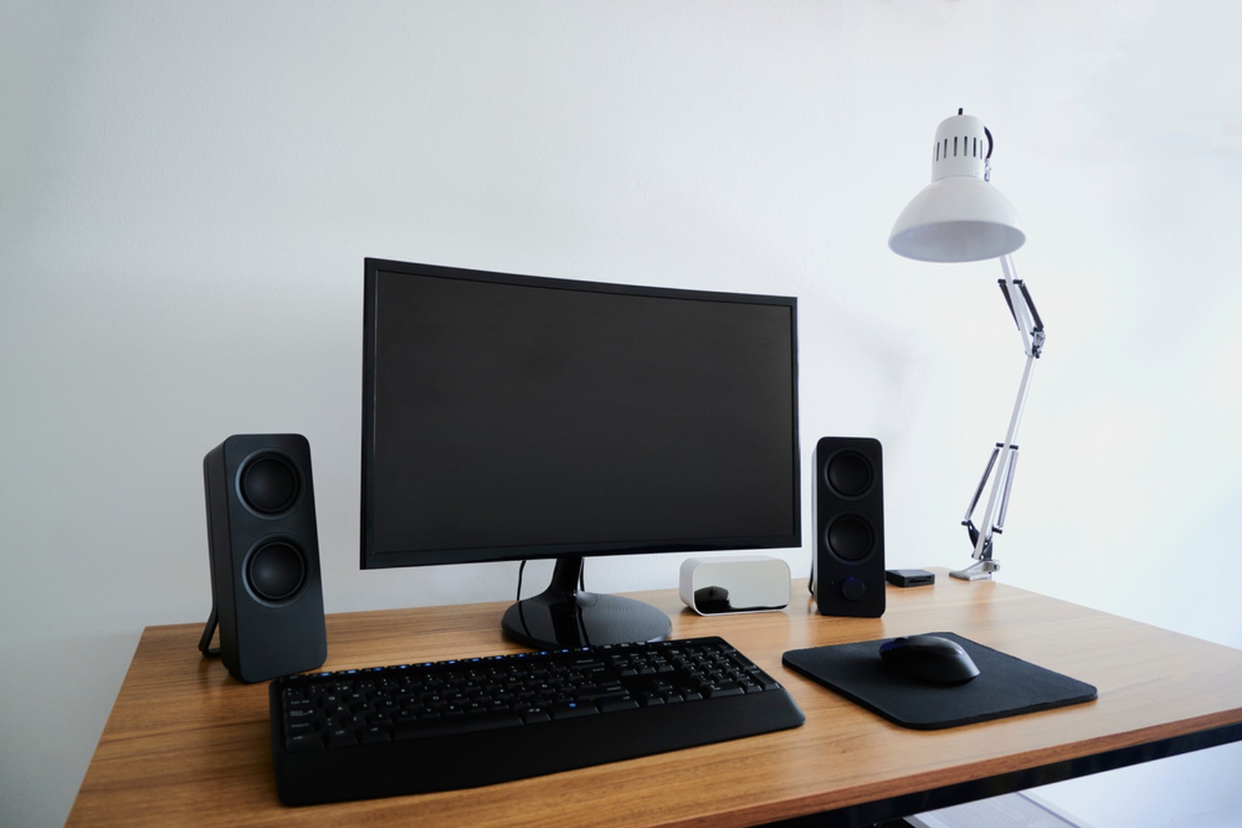 Escritorio de madera con un monitor, teclado, ratón, y altavoces negros y un flexo blanco