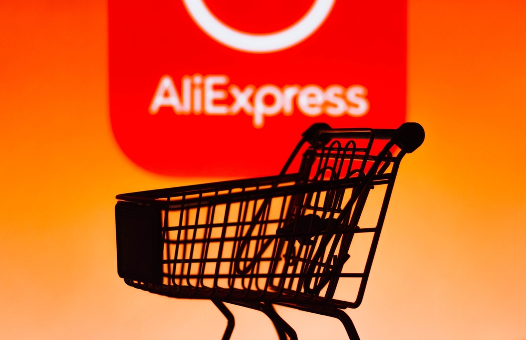 Fondo naranja con el logo de AliExpress y en primer plano un carrito de la compra en contraluz