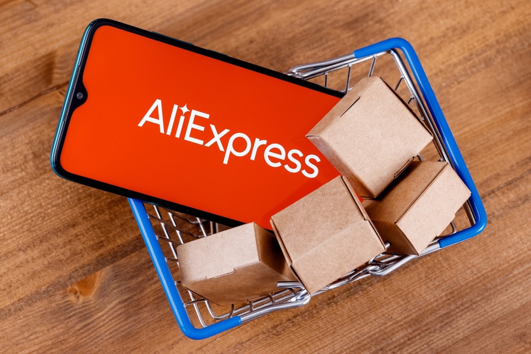 Cesta de la compra con 4 paquetes de cartón pequeños y un smartphone con el logo de AliExpress en pantalla