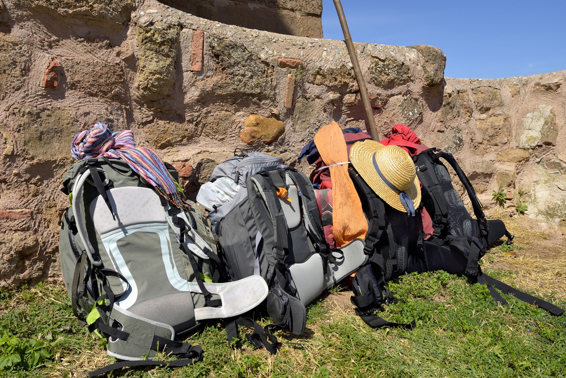 Varias mochilas de peregrino apoyadas en un muro de roca sobre el cesped verde