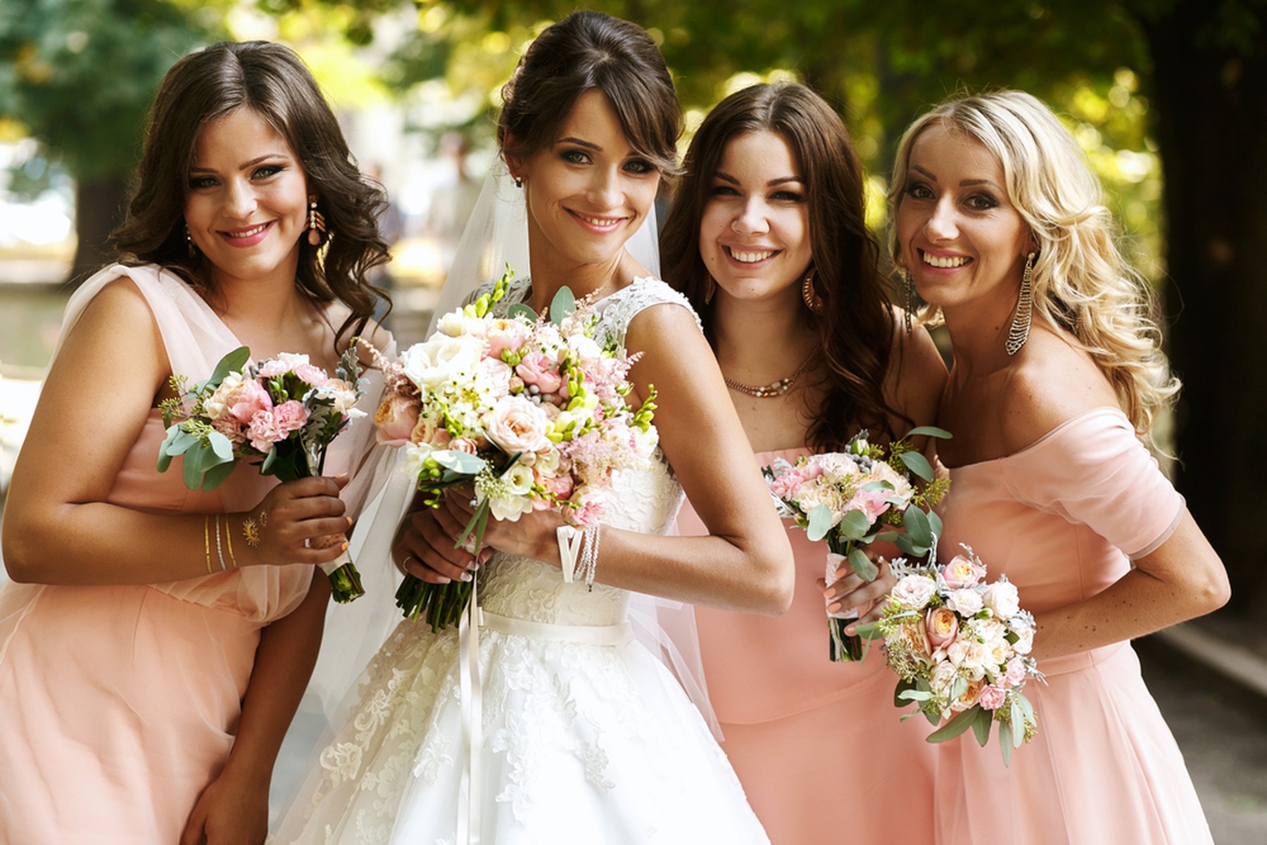 Una mujer joven vestida de novia y sus tres damas de honor con vestidos rosas y ramos de flores en las manos