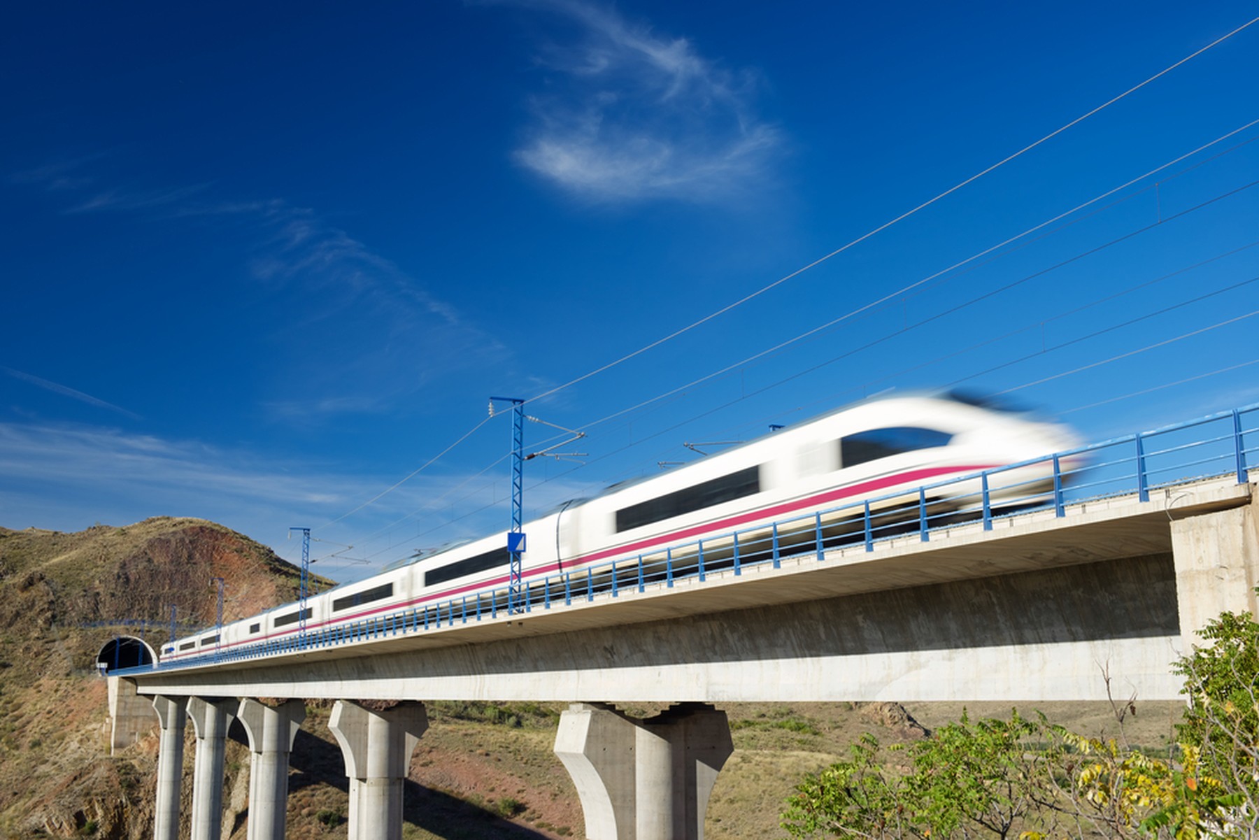 Tren AVE en movimiento saliendo de un túnel con un cielo azul espléndido