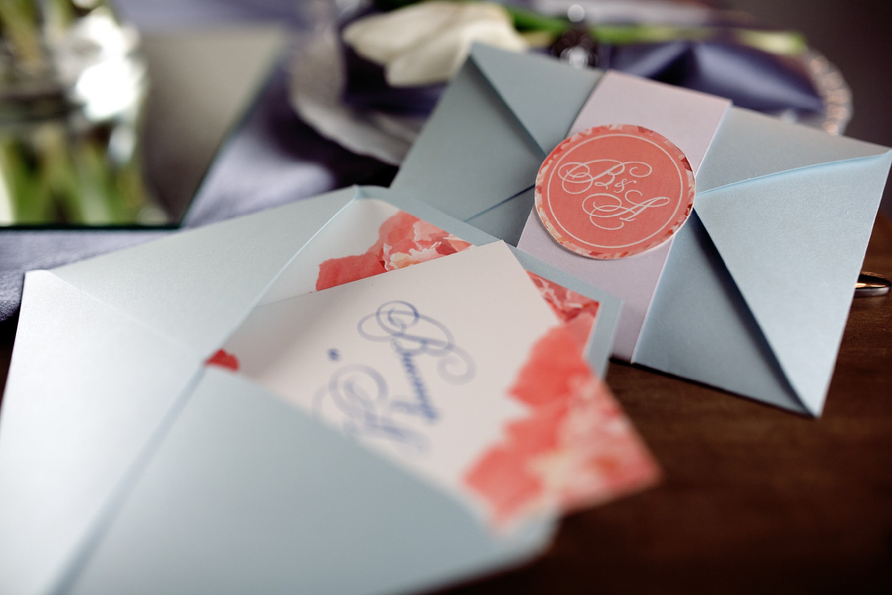 Invitaciones de boda con el sobre azul y un faldón blanco con un sello rosa. Uno de los sobres está abierto y asoma la invitación