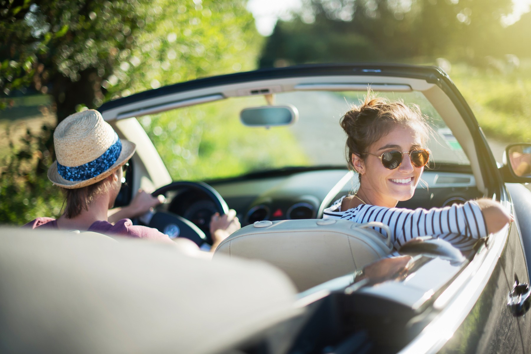 Dos chicas jóvenes en un coche descapotable. La copiloto está mirando hacia atrás sonriendo con unas gafas de sol.