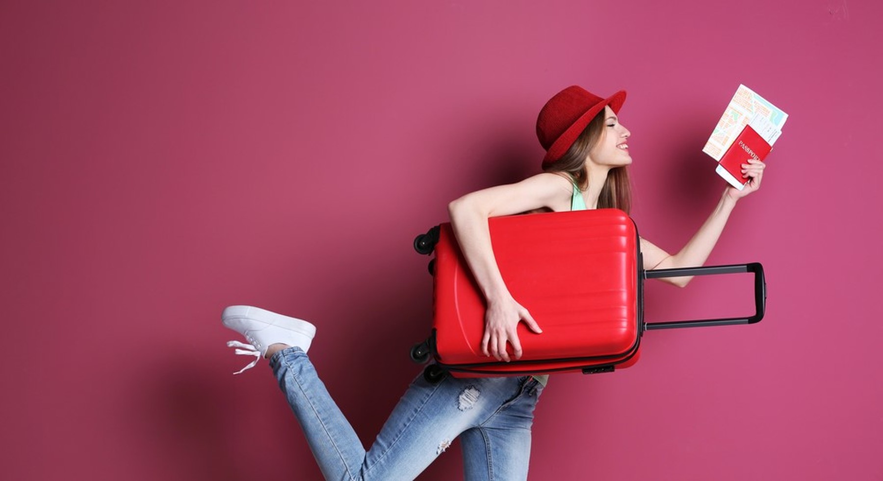 Mujer joven con un gorro rojo. Bajo un brazo lleva una maleta de mano roja también y en la otra mano sostiene un pasaporte y unos billetes de avión.