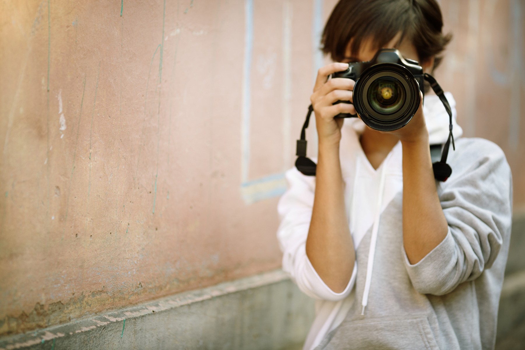 Mujer fotógrafa con una cámara réflex en las manos. Lleva una sudadera gris y blanca.